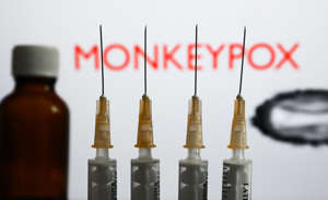 Medical syringes and a bottle are seen with 'Monkeypox' sign and monkeypox illustrative model displayed on a screen in the background in this illustration photo taken in Krakow, Poland on May 26, 2022. (Photo by Jakub Porzycki/NurPhoto via Getty Images)