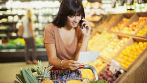 young woman phone browses grocery list supermarket cart_iStock-521813053
