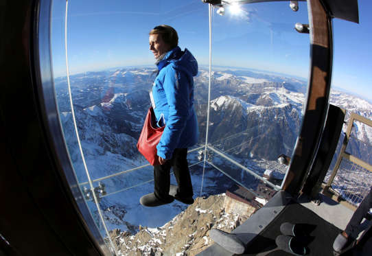 A reporter looks at the mountains through a glass cage named 'Pas dans le Vide' (Step into the Void) at the top of the Aiguille du Midi peak (3842-meters high or 12,604 feet), in the French Alps, during a press visit. Visitors can enjoy the view of Mont Blanc, Europe's highest mountain, from the platform.