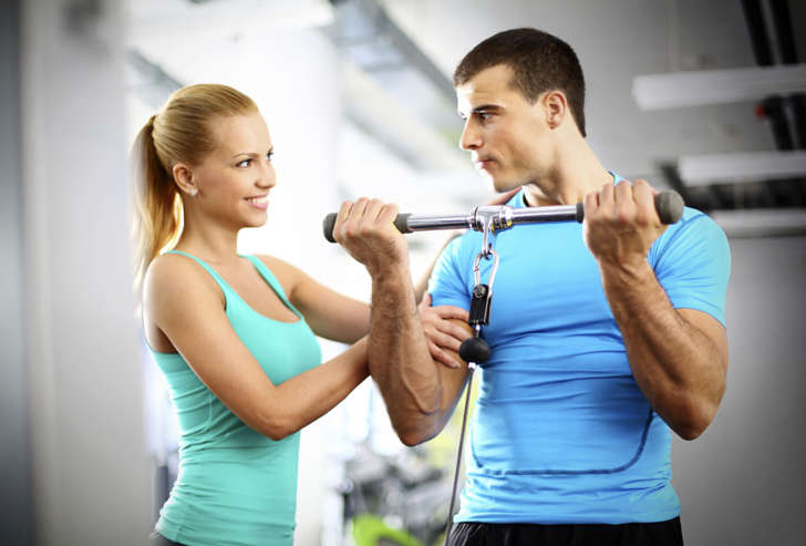 Woman at gym touches a guy's biceps during his workout.