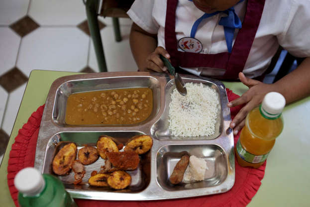 Folie 8 von 20: Milagro Ramos, a student at the Angela Landa elementary school, spoons up rice from her lunch tray, which also contains a chicken croquette, a piece of taro root and yellow pea soup in Old Havana, Cuba, Tuesday, May 6, 2014. Milagro brought fried plantains, lower left corner of her tray, and an orange drink from home. The children provide their own drinks. (AP Photo/Franklin Reyes)