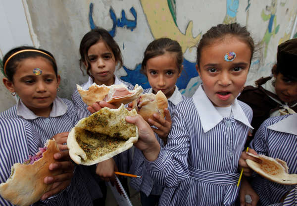 Folie 11 von 20: Palestinian students hold up their sandwiches of pita bread stuffed with olive oil and zaatar, a mixture of herbs and spices, brought from home, during their half-hour mid-day break at about 11 a.m. in the West Bank city of Nablus, Tuesday, May 6, 2014. Palestinian children in the West Bank usually eat during recess in the schoolyard, as there are no dining rooms in schools. (AP Photo/Majdi Mohammed)