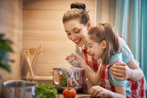 Healthy food at home. Happy family in the kitchen. Mother and child daughter are preparing on the cooker.