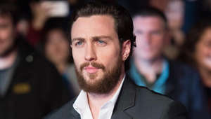 Aaron Taylor-Johnson wearing a suit and tie smiling and looking at the camera