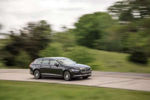 a person riding on the back of a car going down the road: 2021 Volvo V90 T6 AWD