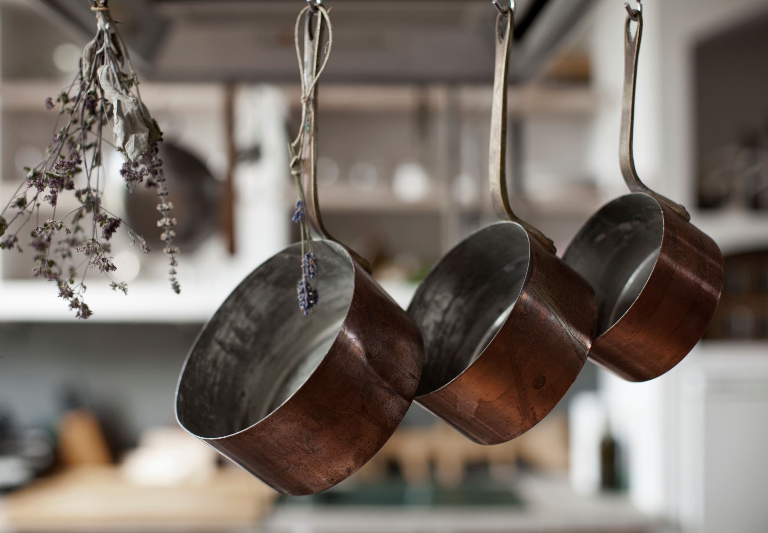 Three saucepans hanging from hooks with dried lavender