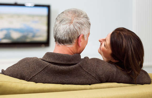 Mature couple sitting on sofa watching television.