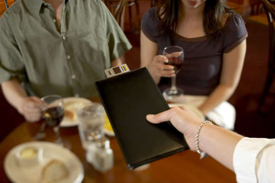 Waitress handing bill to couple in restaurant