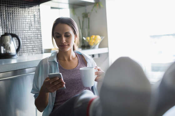 Woman drinking coffee and texting with feet up