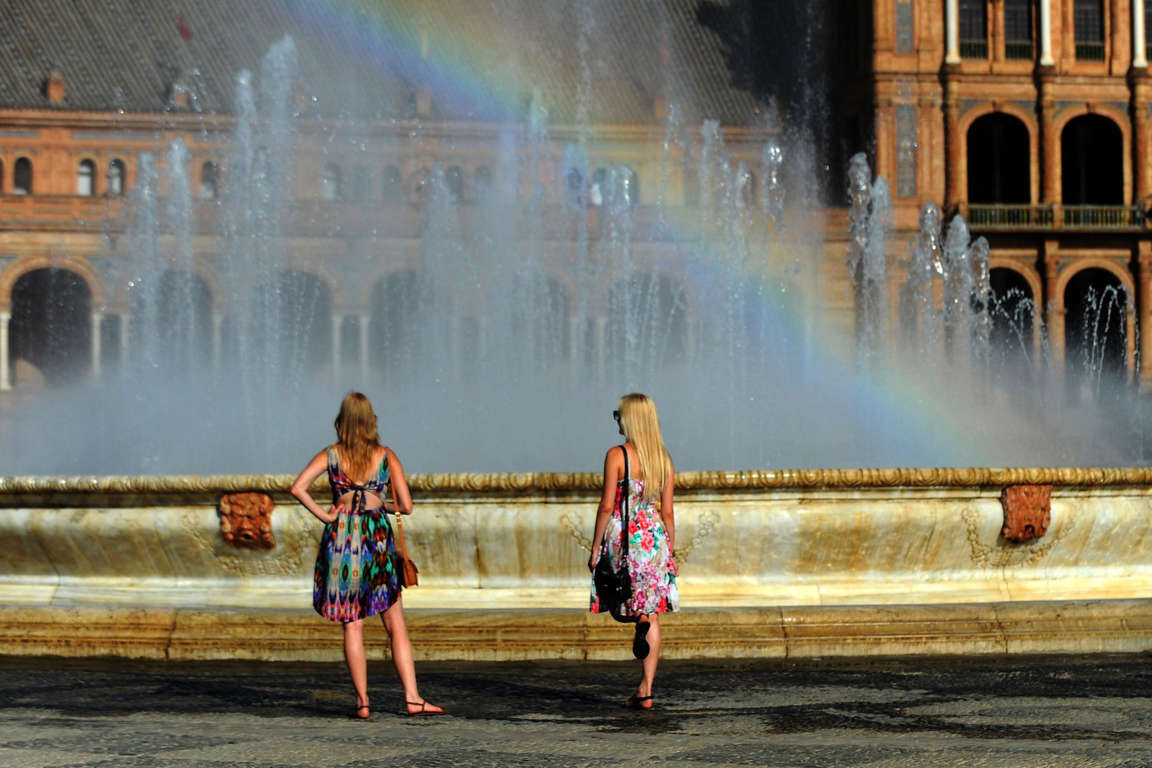 A rainbow comes from a fountain as two women cool off at the Plaza de Espana square in Sevilla on July 8, 2015. A "long-term" new heat wave, that arrives from North Africa and is expected to last at least until July 12, follows a first episode of intense heat at the end of June that led the Meteorological Agency to put 40 of the 50 Spanish provinces in  " yellow " or "orange" alert.