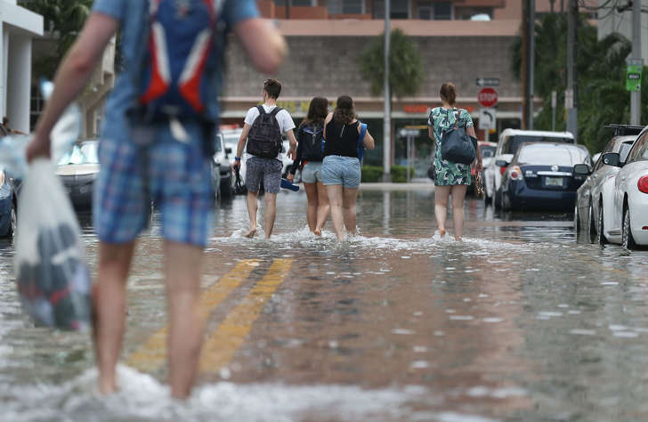 MIAMI BEACH, FL - SEPTEMBER 29: People walk through a flooded street that was caused by the combination of the lunar orbit which caused seasonal high tides and what many believe is the rising sea levels due to climate change on September 29, 2015 in Miami Beach, Florida. The City of Miami Beach is in the middle of a five-year, $400 million storm water pump program and other projects that city officials hope will keep the ocean waters from inundating the city as the oceans rise even more in the future. (Photo by Joe Raedle/Getty Images)