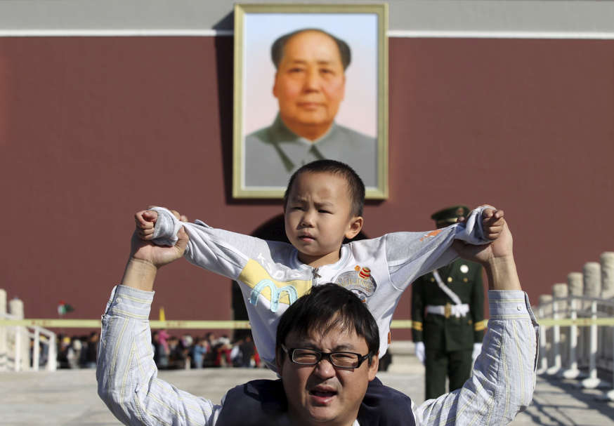 A boy sits on his father's shoulders as they pose for a photograph in front of the giant portrait of late Chinese chairman Mao Zedong on the Tiananmen Gate, in Beijing.<br />