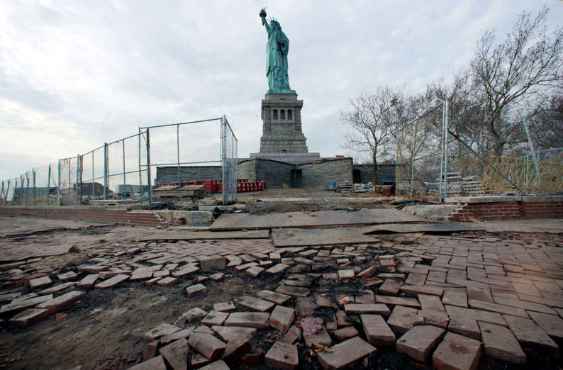 In this Nov. 30, 2012 file photo, the Statue of Liberty stands beyond parts of a brick walkway damaged in Superstorm Sandy on Liberty Island in New York. With scientists forecasting sea levels to rise by anywhere from several inches to several feet by 2100, historic structures and coastal heritage sites around the world are under threat. A multidisciplinary conference is scheduled to convene in Newport, R.I., this week to discuss preserving those structures and neighborhoods that could be threatened by rising seas.