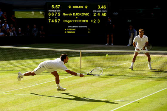 LONDON, ENGLAND - JULY 06:  Novak Djokovic of Serbia dives to make a return as Roger Federer of Switzerland stands at the net during the Gentlemen's Singles Final match on day thirteen of the Wimbledon Lawn Tennis Championships at the All England Lawn Te