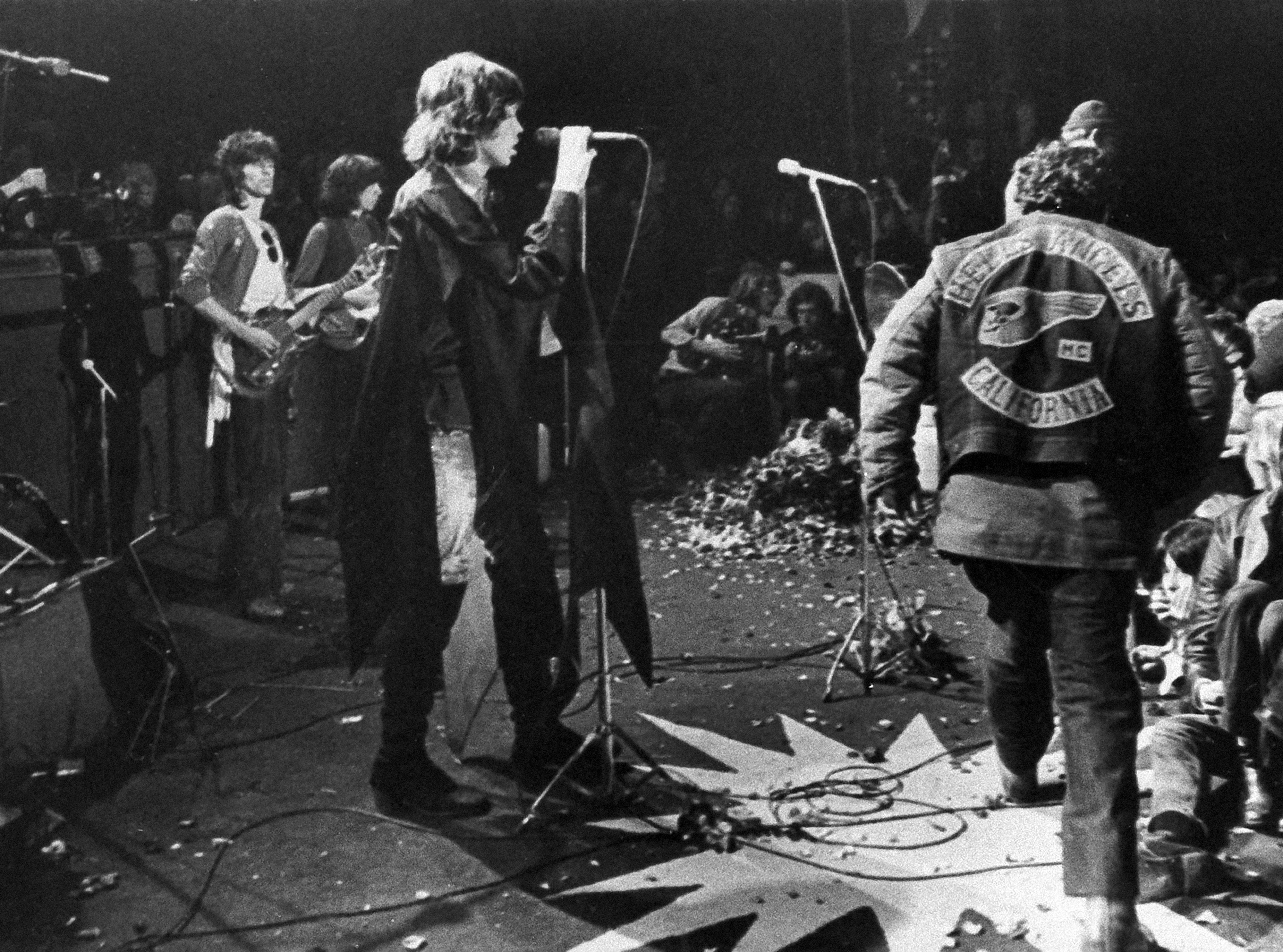 Mick Jagger sings at the Altamont Rock Festival at Livermore, Calif. on Saturday, December 6, 1969 while Hells Angels cross stage during melee to help fellow motorcyclists. The Rolling Stone hired the Hells Angels to police the concert for $500 worth of beer.