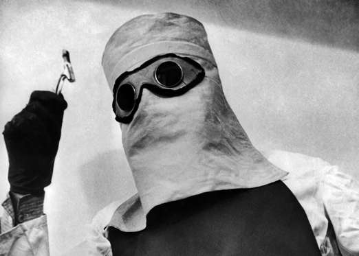 Slide 4 of 15: A doctor wearing a mask, shirt and apron impregnated with lead to shield him from the effects of a vial of radium in 1936.