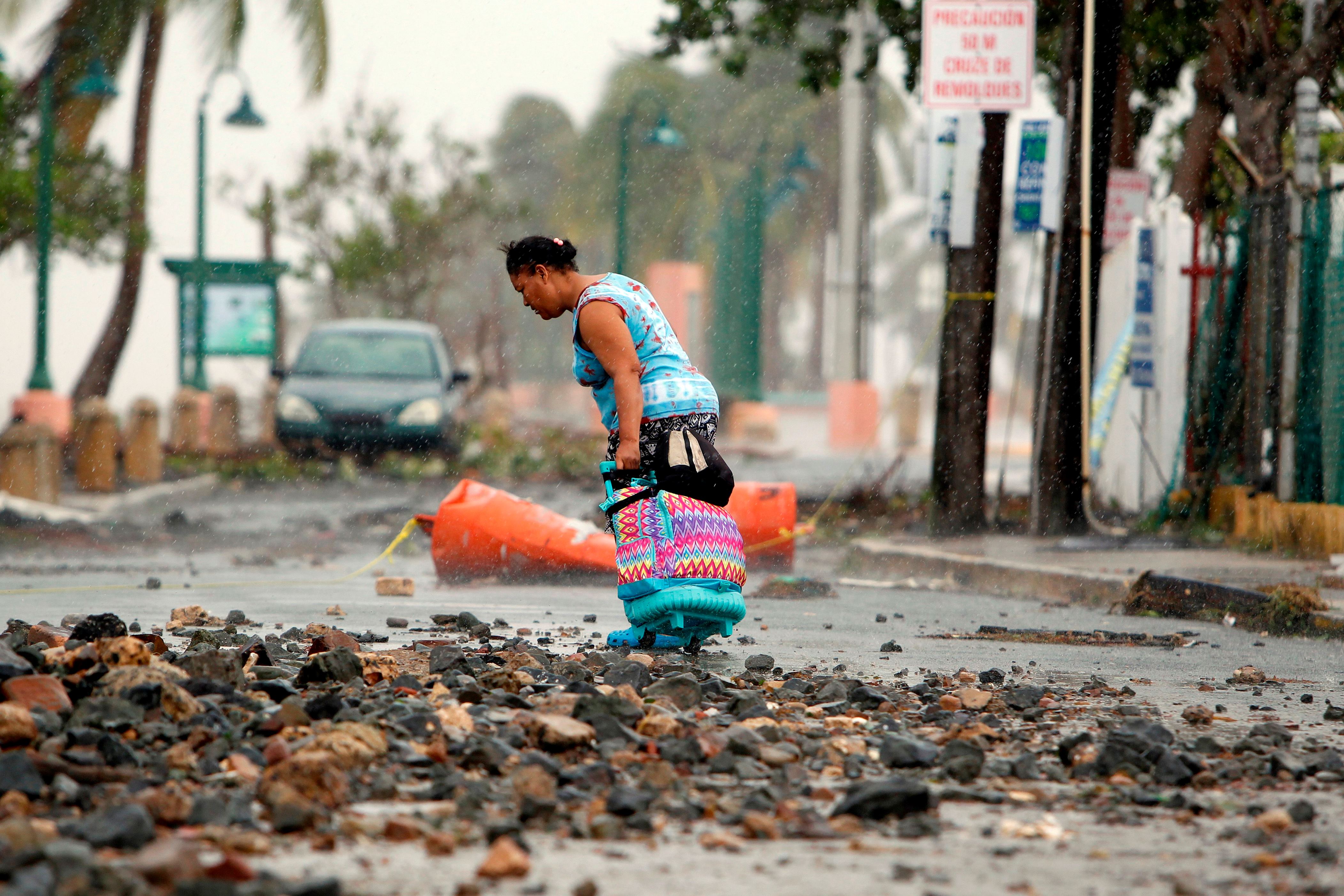 TOPSHOT - A woman pulls a travel case on a rock scattered road in the aftermath of Hurricane Irma in Fajardo, Puerto Rico, on September 7, 2017. One of the most powerful Atlantic storms on record, the rare Category 5 hurricane churned westward off the northern coast of Puerto Rico early Thursday on a potential collision course with south Florida, where at-risk areas were evacuated. / AFP PHOTO / Ricardo ARDUENGO (Photo credit should read RICARDO ARDUENGO/AFP/Getty Images)