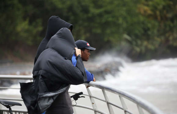 Slide 3 of 20: A woman covers herself with a raincoat while looking out at the ocean as Hurricane Maria approaches in Guadeloupe island, France