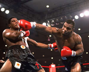 a man doing a trick on a stage: Mike Tyson delivers a blow to Trevor Berbick during a boxing match in 1986.