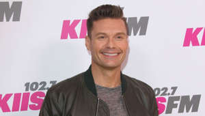 Ryan Seacrest holding a sign posing for the camera