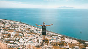 a person standing on a rocky beach next to a body of water: This Mediterranean country announced it will finally be opening its borders on May 14, Zapatka said. “Since that announcement, they have already seen accommodation in places like Mykonos and Santorini swell to 70% capacity,” Zapatka said. For now, travelers will either need to show proof of vaccination or a negative PCR test, one or the other. For the budget-minded, Zapatka said Greece is “a very budget-friendly destination.” He states that an average trip cost for two travelers for 8-10 days could be as low as $3,000 including three-star accommodations, transportation and great food options. Read: How To Plan Future Travel Without Risking Your Deposits