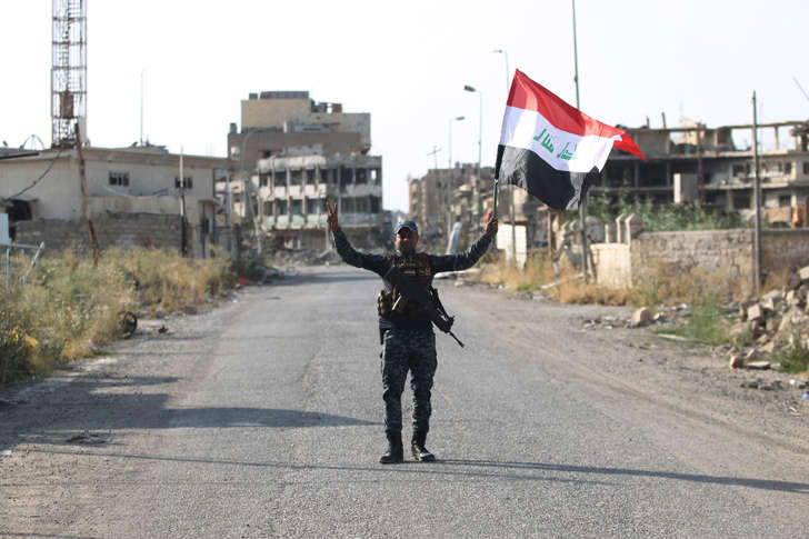 An Iraqi federal police member waves his country's national flag as he celebrates in the Old City of Mosul on July 9, 2017 after the government's announcement of the 'liberation' of the embattled city.
