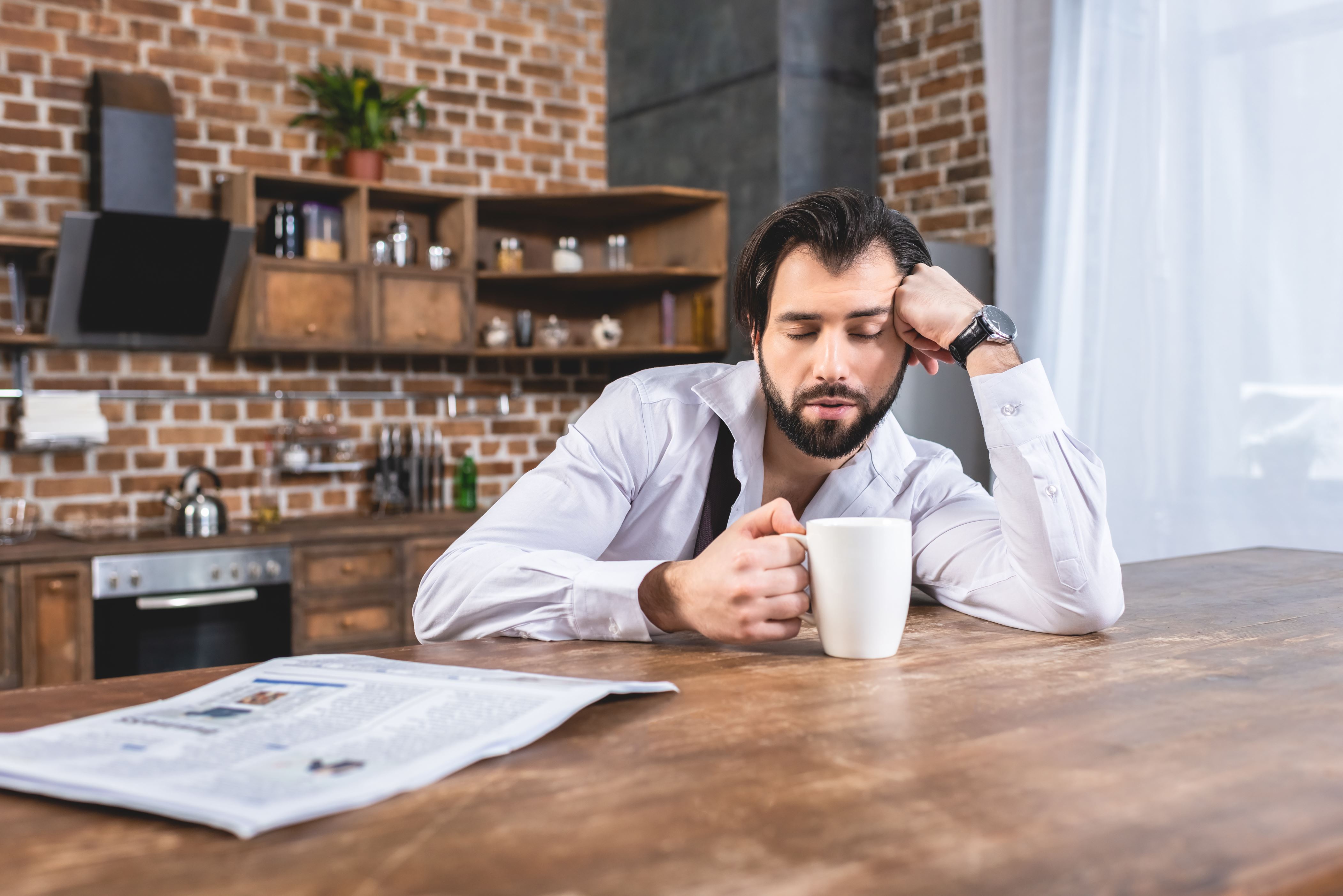 Slide 1 of 13: handsome loner businessman sitting with cup of coffee and sleeping at table at kitchen