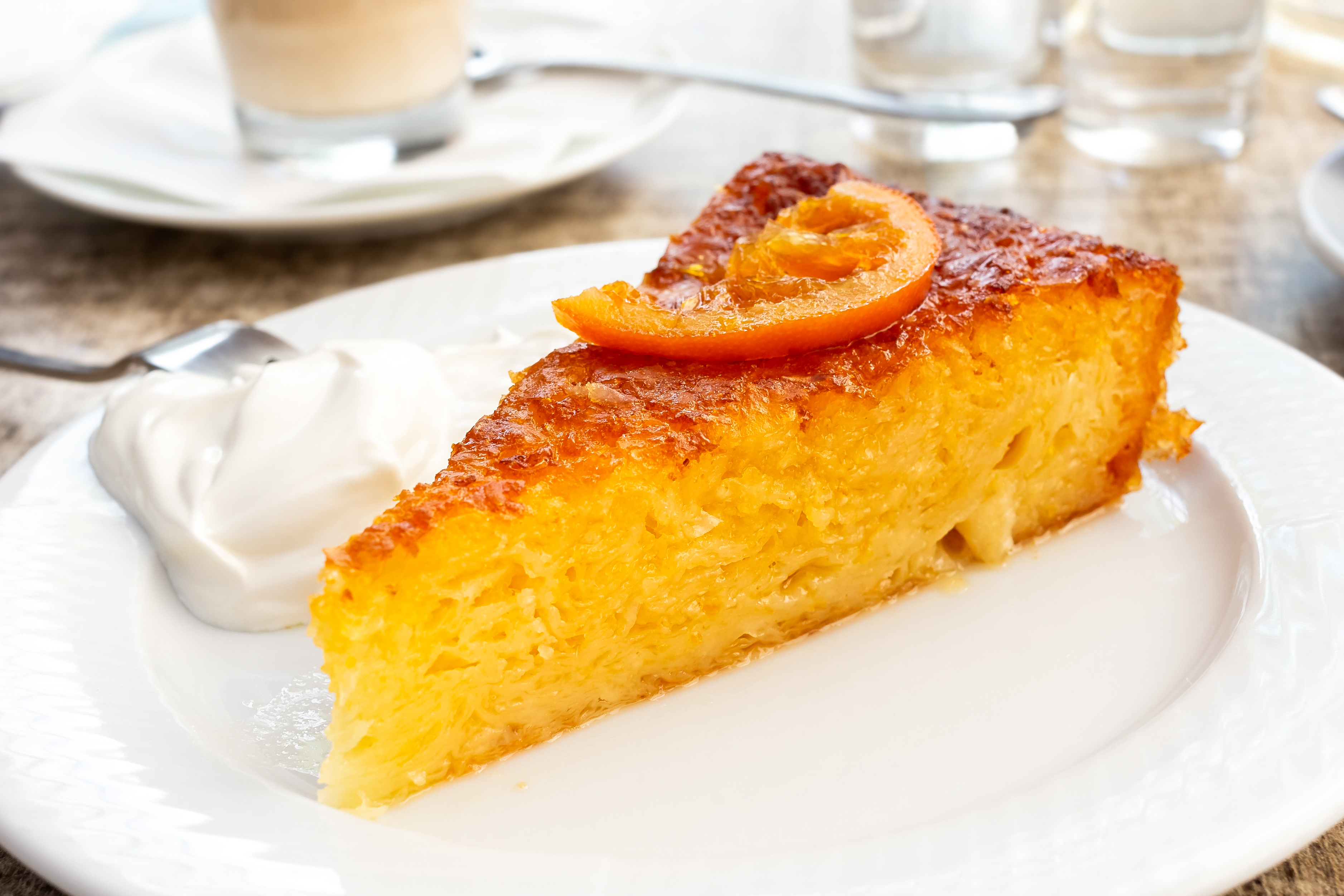 A piece of traditional greek orange cake with sour cream on white plate.