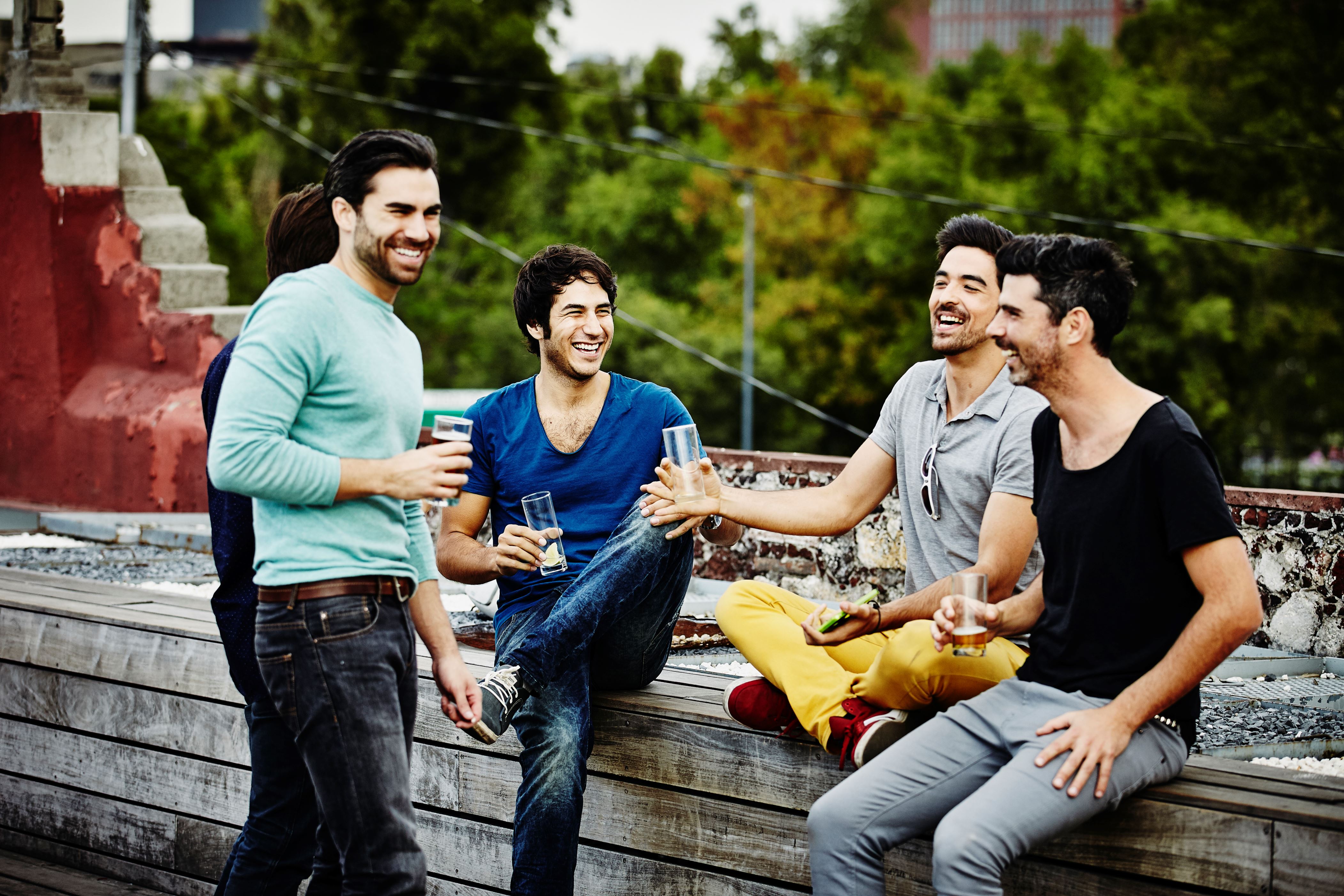 Laughing group of friends sharing drinks on rooftop deck