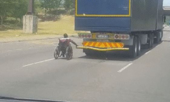 Man in Wheelchair Grips Back of Truck as it Speeds Down South African Highway