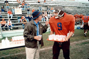 a man standing in front of a crowd: A bullied college waterboy (Adam Sandler, with Henry Winkler) finally gets in the game as a football wunderkind in "The Waterboy."