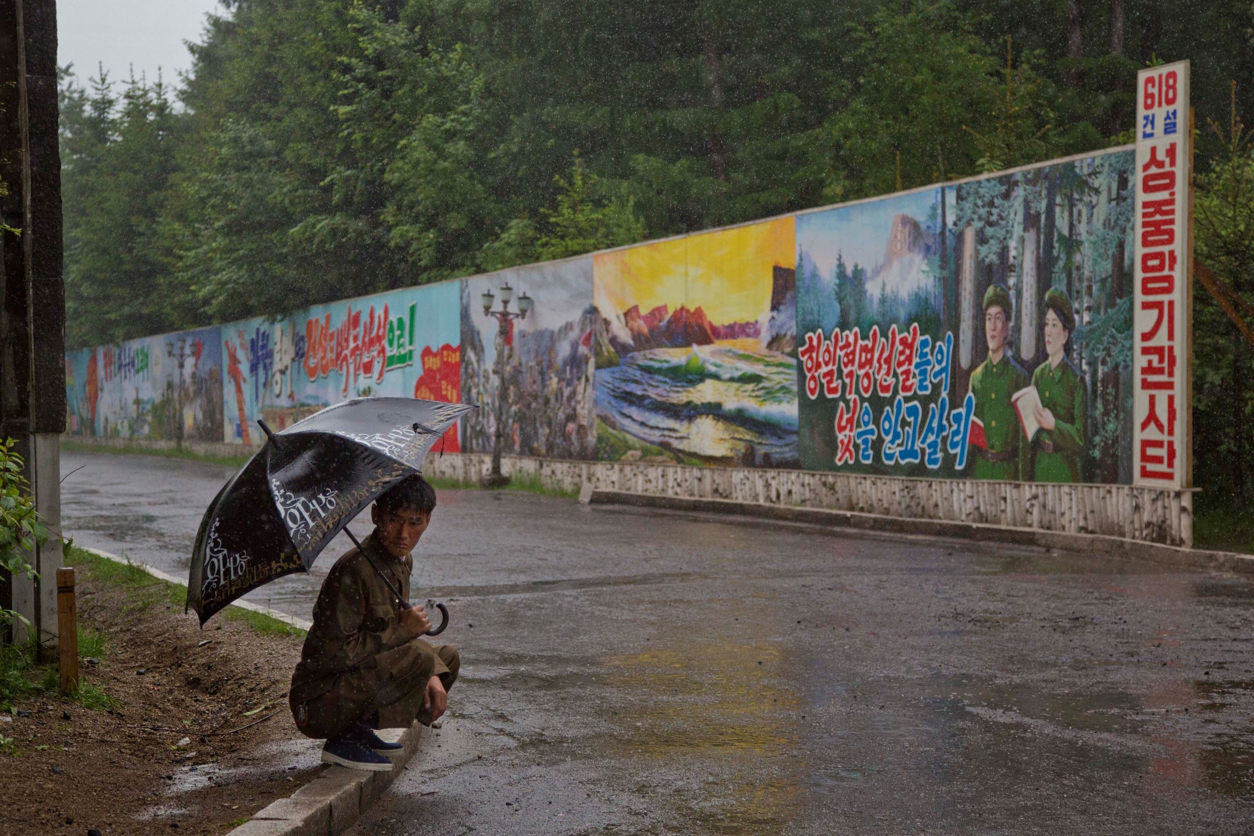 A man takes shelter in the rain next to long propaganda billboards in the town of Samjiyon in North Korea's Ryanggang province.