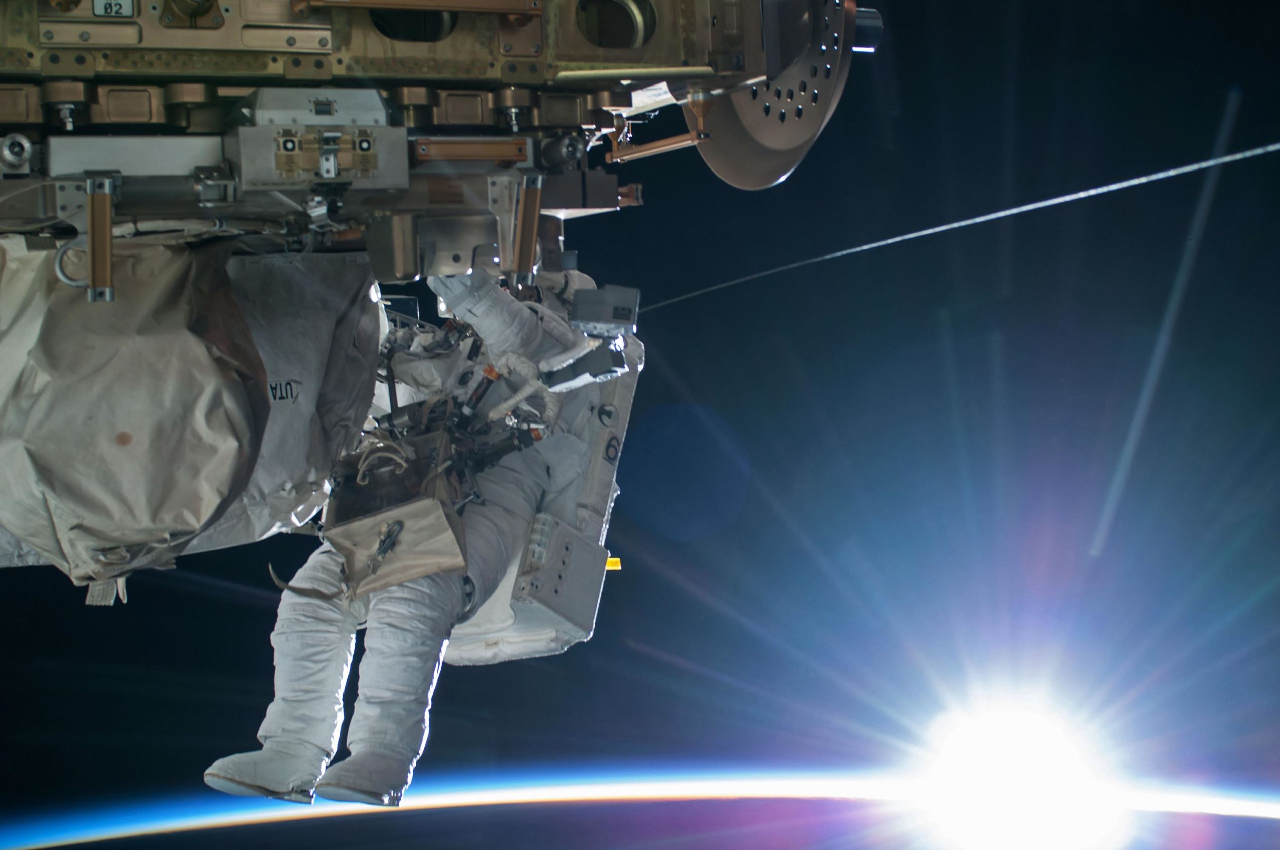 NASA astronaut Terry Virts Flight Engineer of Expedition 42 works to complete a cable routing task while the sun begins to peak over the Earth's horizon on the International Space Station. Virts and fellow astronaut Barry "Butch" Wilmore completed a 6-hour, 41-minute spacewalk routing more than 300 feet of cable as part of a reconfiguration of the station to enable U.S. commercial crew vehicles under development to dock to the space station in the coming years.