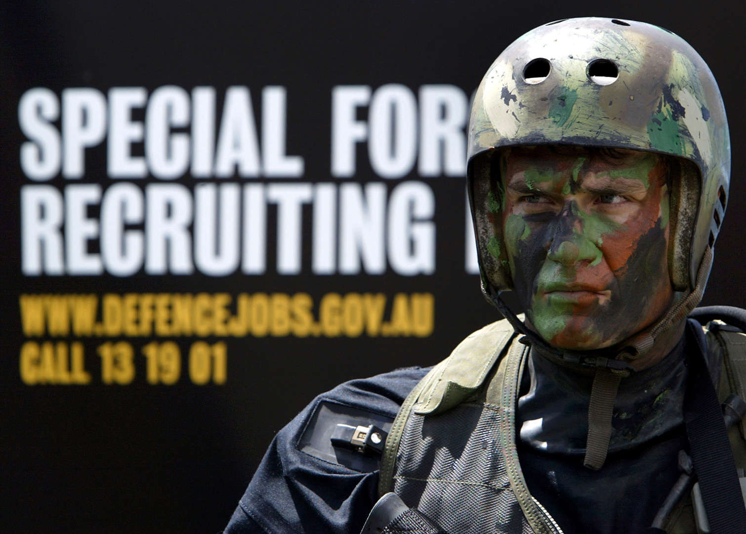 A Special Air Services (SAS) oldier stands in front of a recruitment poster in Sydney October 20, 2003 after a demonstration of their skills as part of a public recruitment drive for more than 300 elite SAS troops by the defense force in order to bolster defense capabilities due to the war on terror. The break with tradition of only recruiting elite soldiers from within defense ranks was necessary to fill an extra 334 commando places announced by the government earlier in the year.