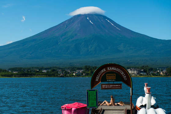 Tourists sunbathe on a pier on Lake Kawaguchiko as Mount Fuji stands behind the lake in Fujikawaguchiko, Yamanashi Prefecture, Japan.