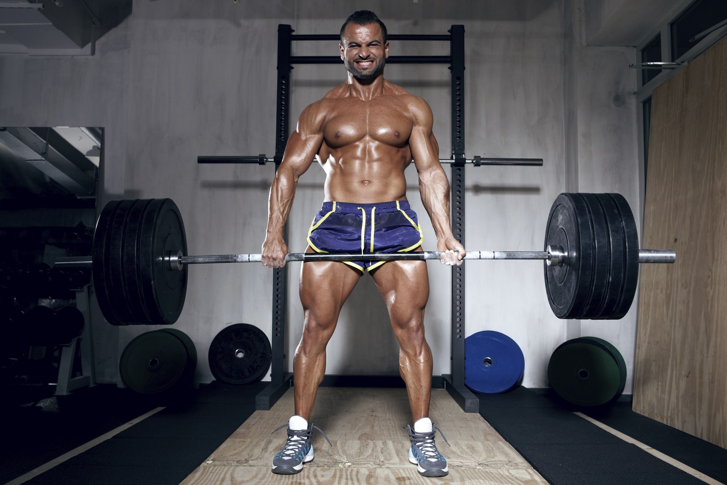 male muscular Bodybuilder performing dead Lifts with a lot of weights in a gym