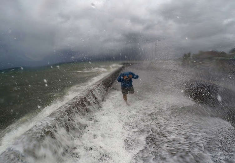 A resident walks past big waves spilling over a wall onto a coastal road in the city of Legaspi in Albay province, south of Manila on December 14, 2015, as typhoon Melor approaches the city. More than 700,000 people fled the central Philippines amid threats of giant waves, floods and landslides as powerful Typhoon Melor approached the archipelago nation, officials said December 14.