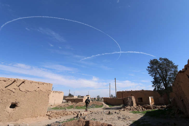 A Syria Democratic Forces fighter walks under contrails made by U.S. alliance air forces on the outskirts of al-Shadadi town, Hasaka countryside, Syria February 19, 2016.