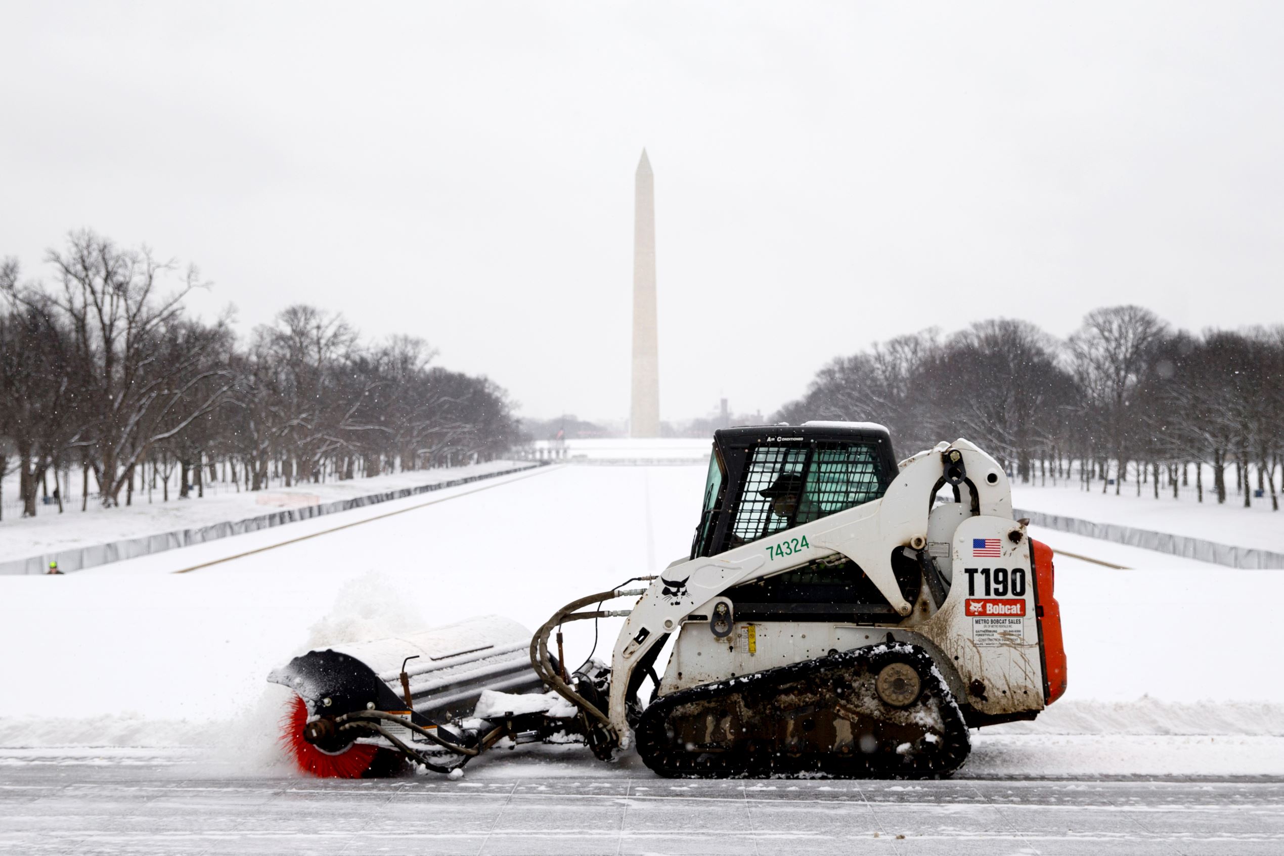 A worker with the National Park Service brushes snow from in front of the Lincoln Memorial as the Washington Monument is seen in the distance on Feb. 15, 2016, in Washington, DC.
