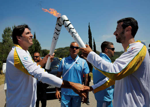 The Olympic flame’s second torch bearer, Brazil’s Giovane Gavio, passes the flame to Greek rower Dimitrios Mougios.