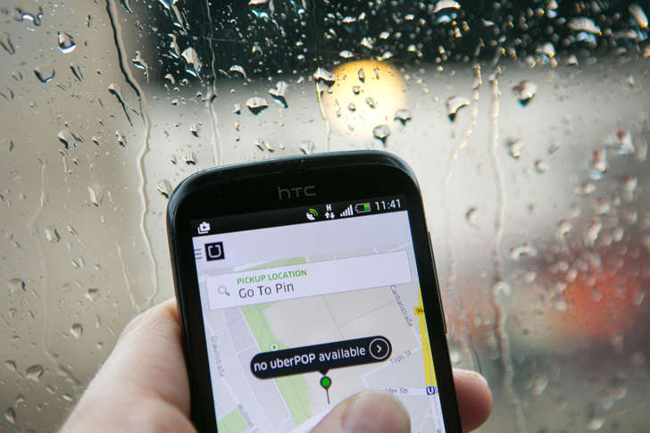 Smartphone displays the Uber Technologies Inc. UberPop car service application (app) as rain streaks an automobile windshield in this arranged photograph in Berlin, Germany on Nov. 24, 2014.