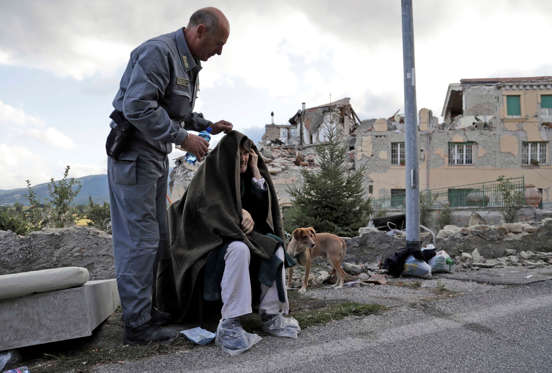 An elderly man is given assistance as collapsed buildings are seen in the background following an earthquake, in Amatrice, Italy, Wednesday, Aug. 24, 2016.  The magnitude 6 quake struck at 3:36 a.m. (0136 GMT) and was felt across a broad swath of central Italy, including Rome where residents of the capital felt a long swaying followed by aftershocks.