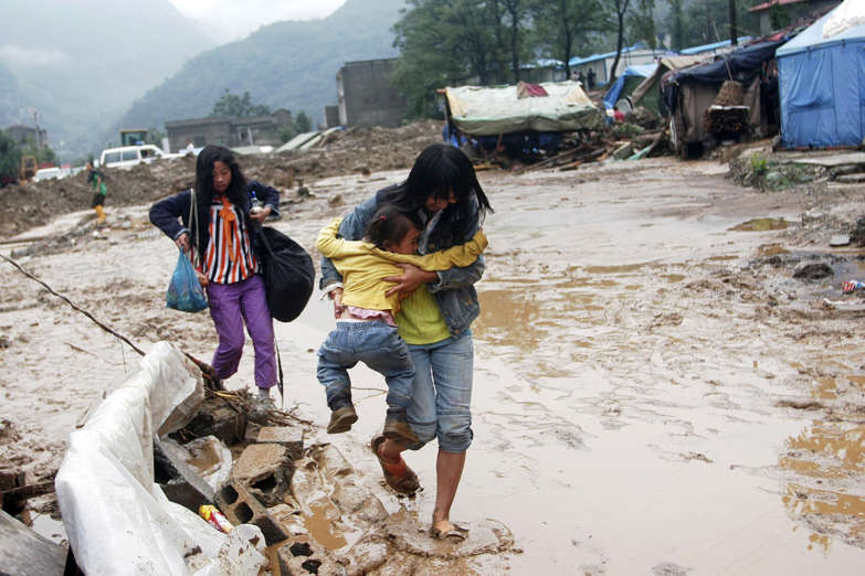 A woman holding her daughter crosses a muddy road after a flash flood caused by torrential rain hit Beichuan, Sichuan province September 25, 2008. Sixteen people have died and 48 others are missing after flash floods and landslides hit an area of southwest China still recovering from a devastating earthquake in May, state media said on Friday. Picture taken September 25, 2008.