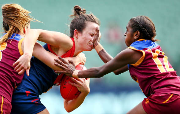 Slide 20 of 34: MELBOURNE, VICTORIA - MAY 22:  Daisy Pearce of Melbourne is tackled by Emily Bates of Brisbane and Delma Gisu of Brisbane during the 2016 AFL Womens match between the Melbourne Demons and the Brisbane Lions at the Melbourne Cricket Ground on May 22, 2016