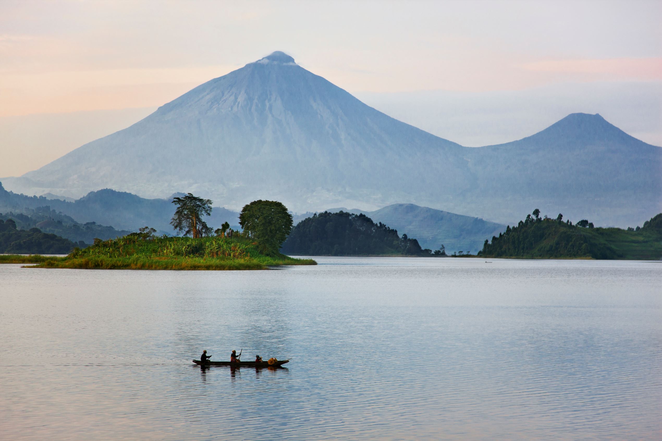 Slide 12 of 20: A man and woman paddle a dugout canoe across Lake Mutanda at sunrise. This lake with its many small 
