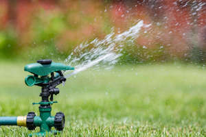 A lawn sprinkler waters the grass in a yard