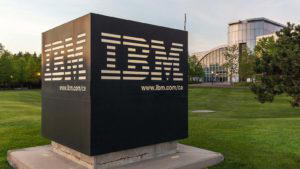 Quantum computing stocks: Sign of IBM with Canada Head Office Building in background in Markham, Ontario, Canada. IBM is an American multinational technology company.