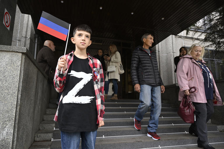 A boy wearing a T-shirt with the letter 'Z', the tactical insignia of Russian troops in Ukraine, and holding a flag of the self-proclaimed Donetsk People's Republic (DNR) - the eastern Ukrainian breakaway region - stands at the entrance to the DNR embassy in Moscow on September 23, 2022, as Moscow-held regions of Ukraine vote in annexation referendums that Kyiv and its allies say are illegal and illegitimate. (Photo by Alexander NEMENOV / AFP) (Photo by ALEXANDER NEMENOV/AFP via Getty Images)
