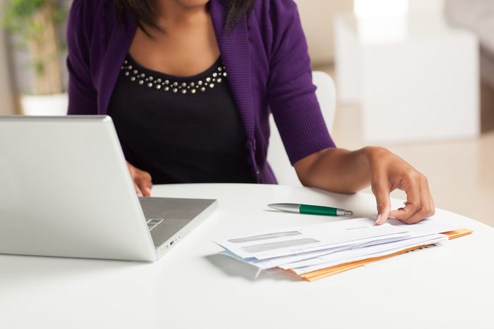 Attractive young African American woman working on finances at home wearing purple jacket sitting at dining table.