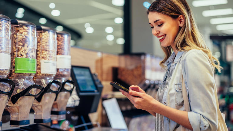 smiling woman checks smartphone grocery store supermarket_iStock-1409433710